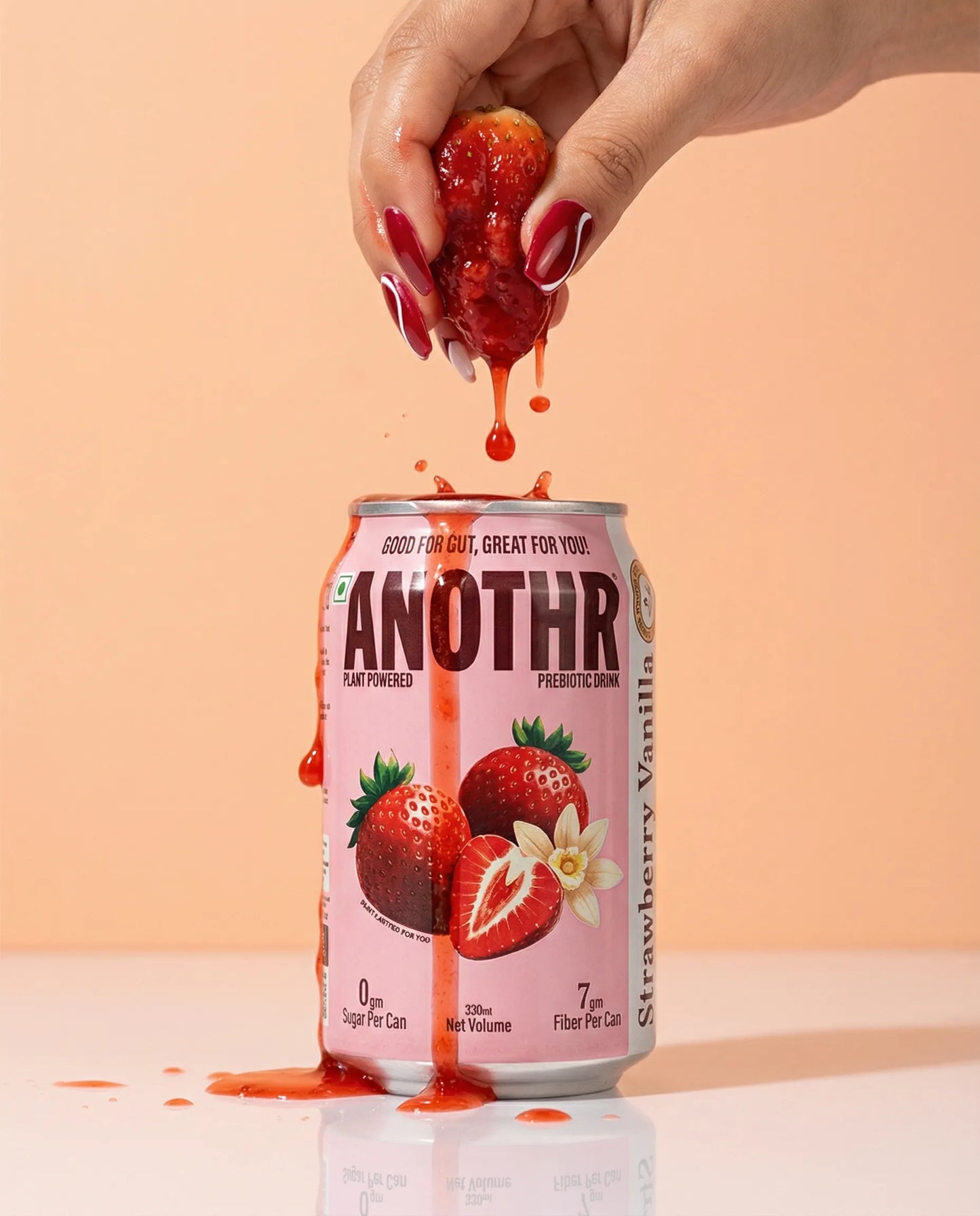 Can of 'ANOTHR Prebiotic Cold Drink' strawberry vanilla soda drink with a strawberry being squeezed over it against a peach background